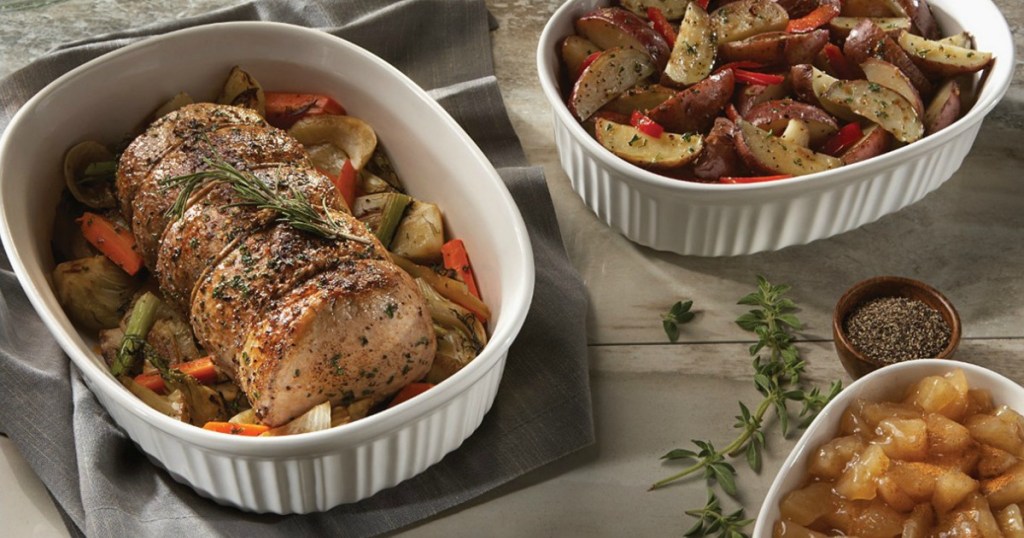 Set of bakeware from Corningware with a pork roast and sides on a wooden counter top