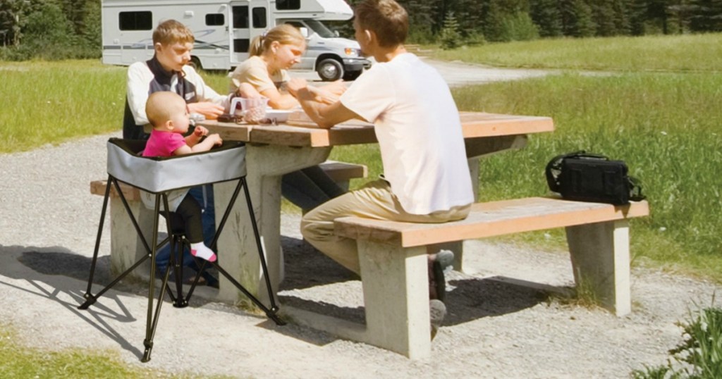 family sitting at campsite with baby in portable dining chair