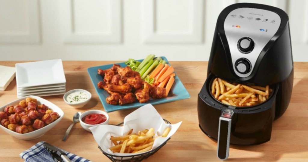 Black air fryer with fries in basket and various appetizers on the countertop