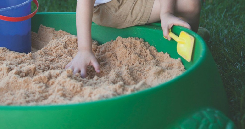 Kid playing in green sandbox with bucket and shovel