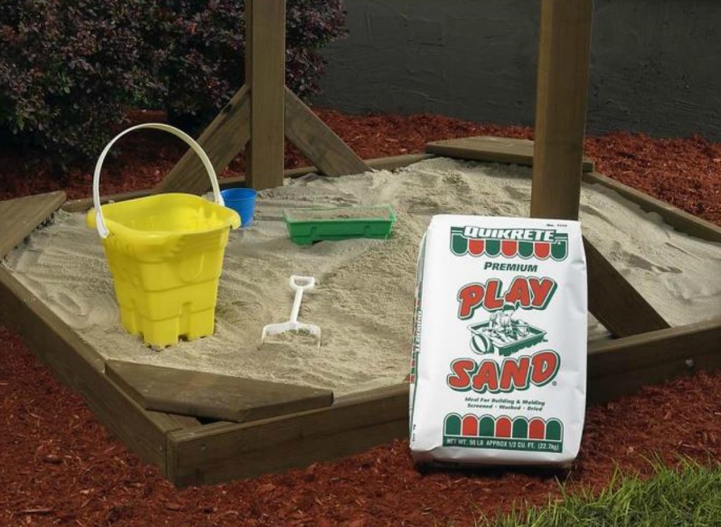 Large bag of play sand in front of a full size sand box with accessories