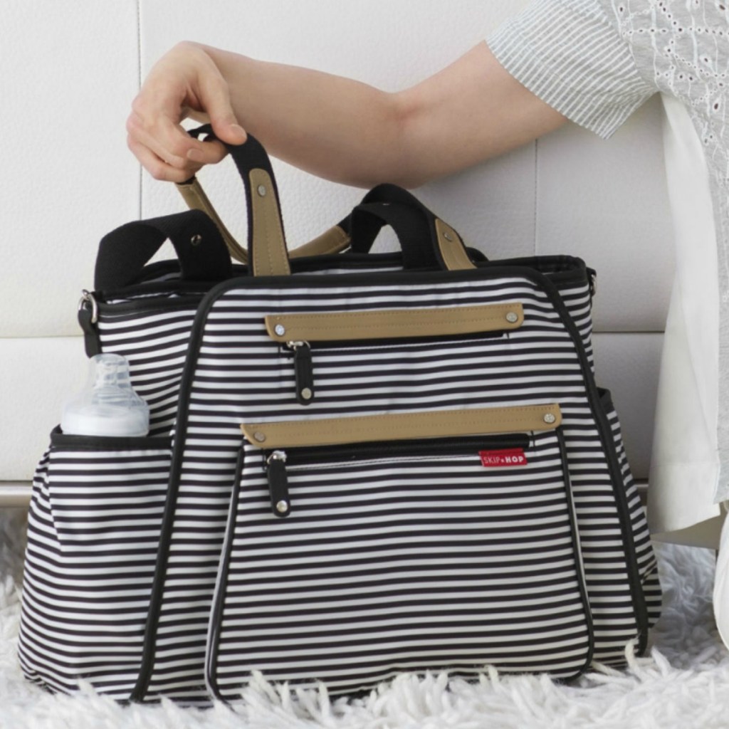 Black and white stripped diaper bag on white faux fur rug near white couch