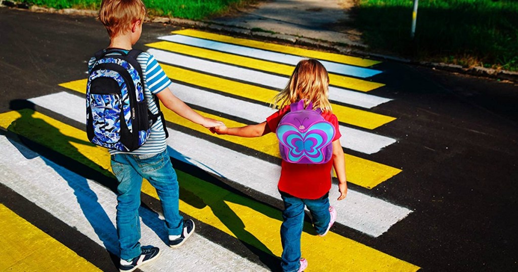 boy and girl holding hands crossing the street wearing backpacks