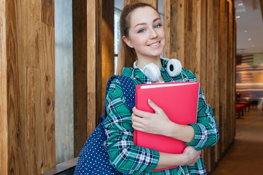 student holding red folder with headphones on neck