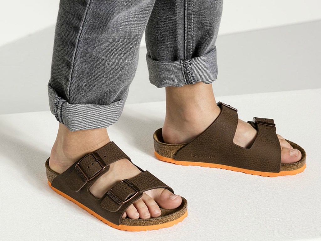 kid in jeans wearing 2 strap brown sandals