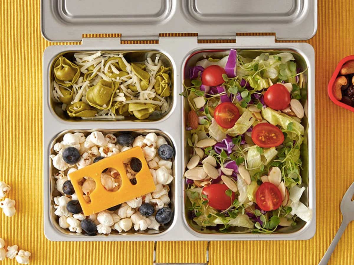 metal lunchbox with pasta, salad, fruit and popcorn filling three onlinepartments