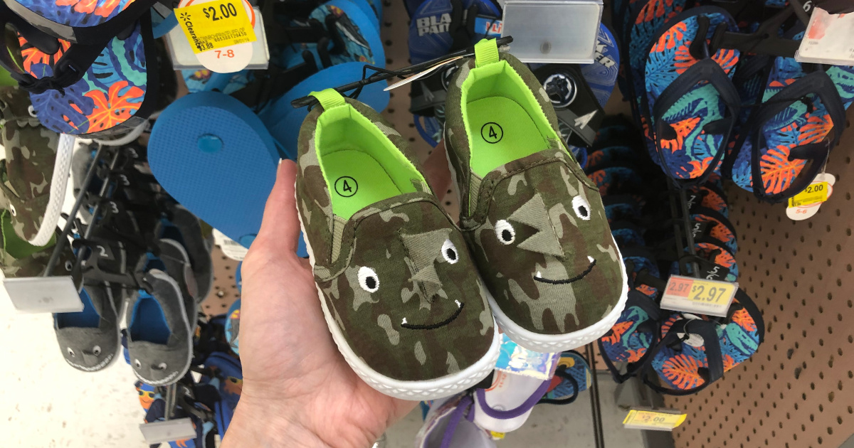 woman holding pair of kids dino shoes in store