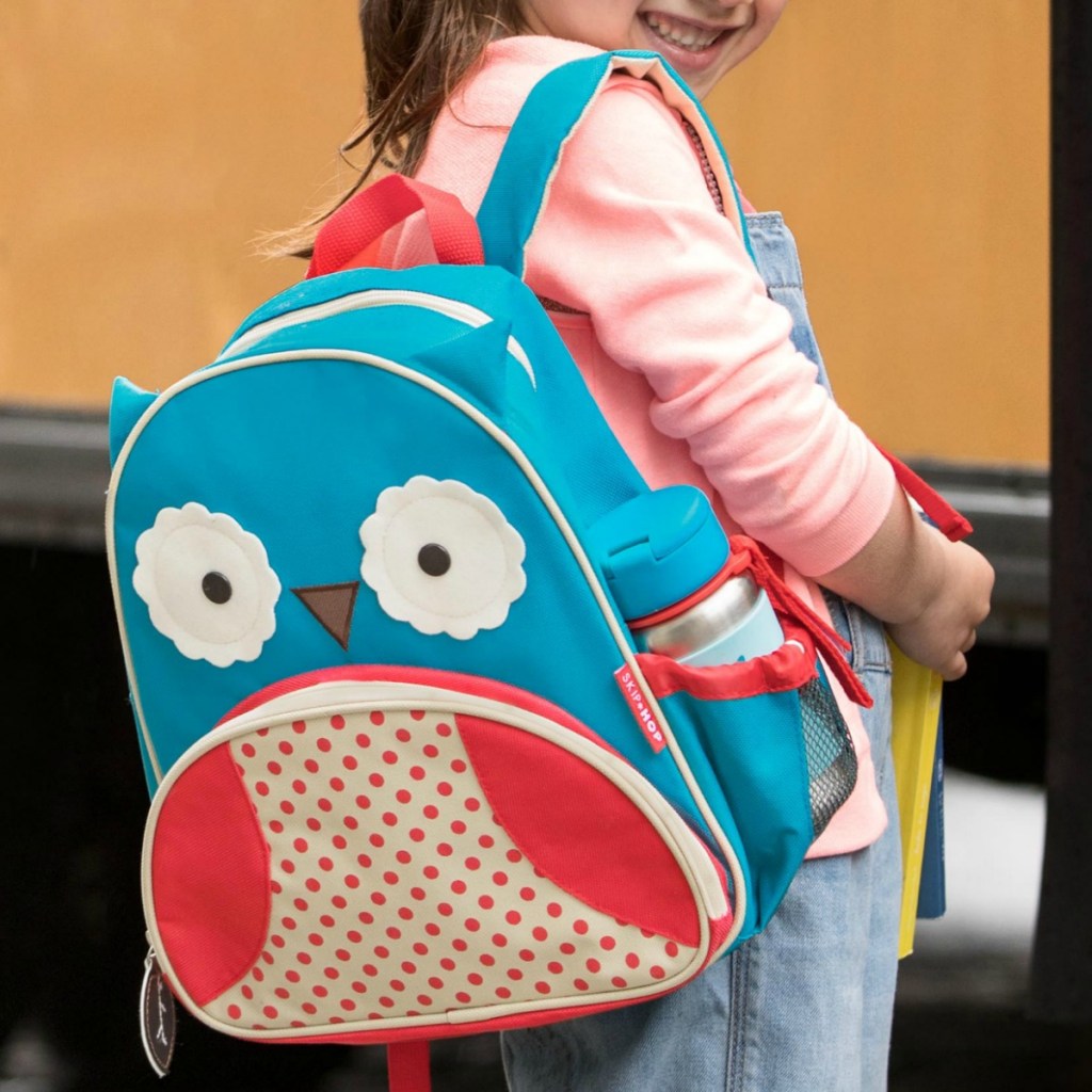 Girl wearing owl themed backpack standing in front of school bus