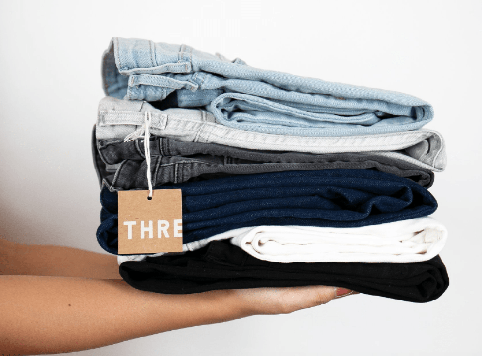 Woman holding stack of jeans with thredUP tag