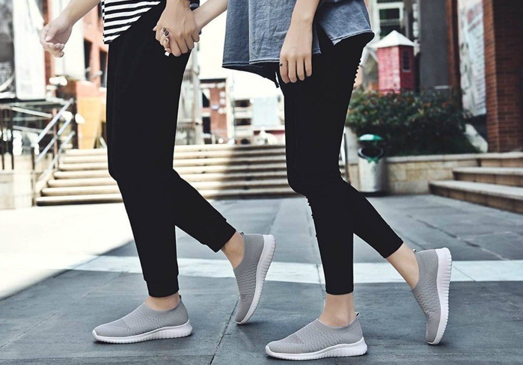 man and woman holding hands while walking and wearing matching gray sneakers