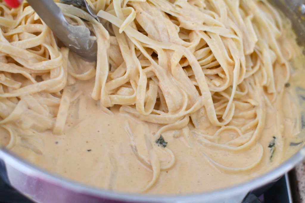 adding fettuccine noodles to pumpkin alfredo sauce