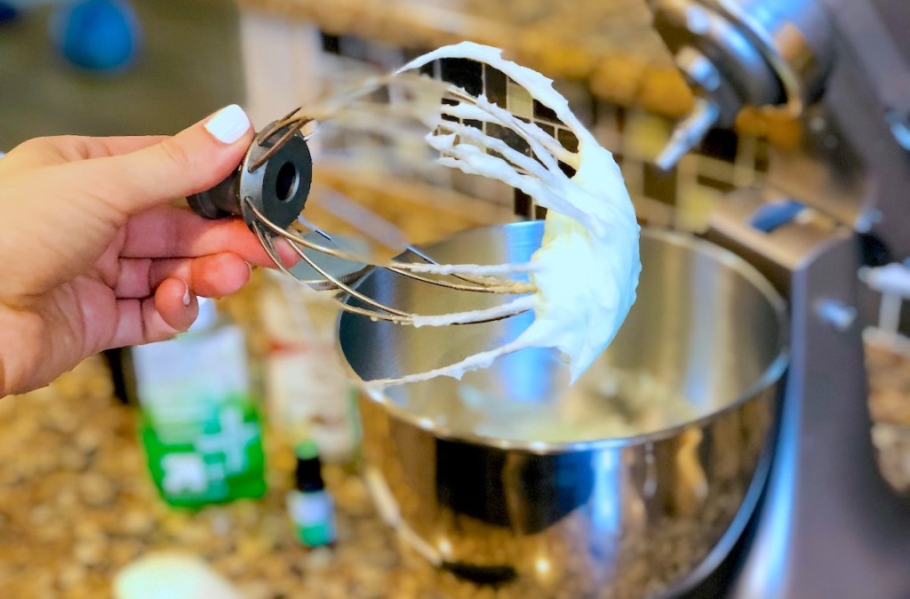 hand holding a whisk with whipped cooling coconut oil lotion on tip