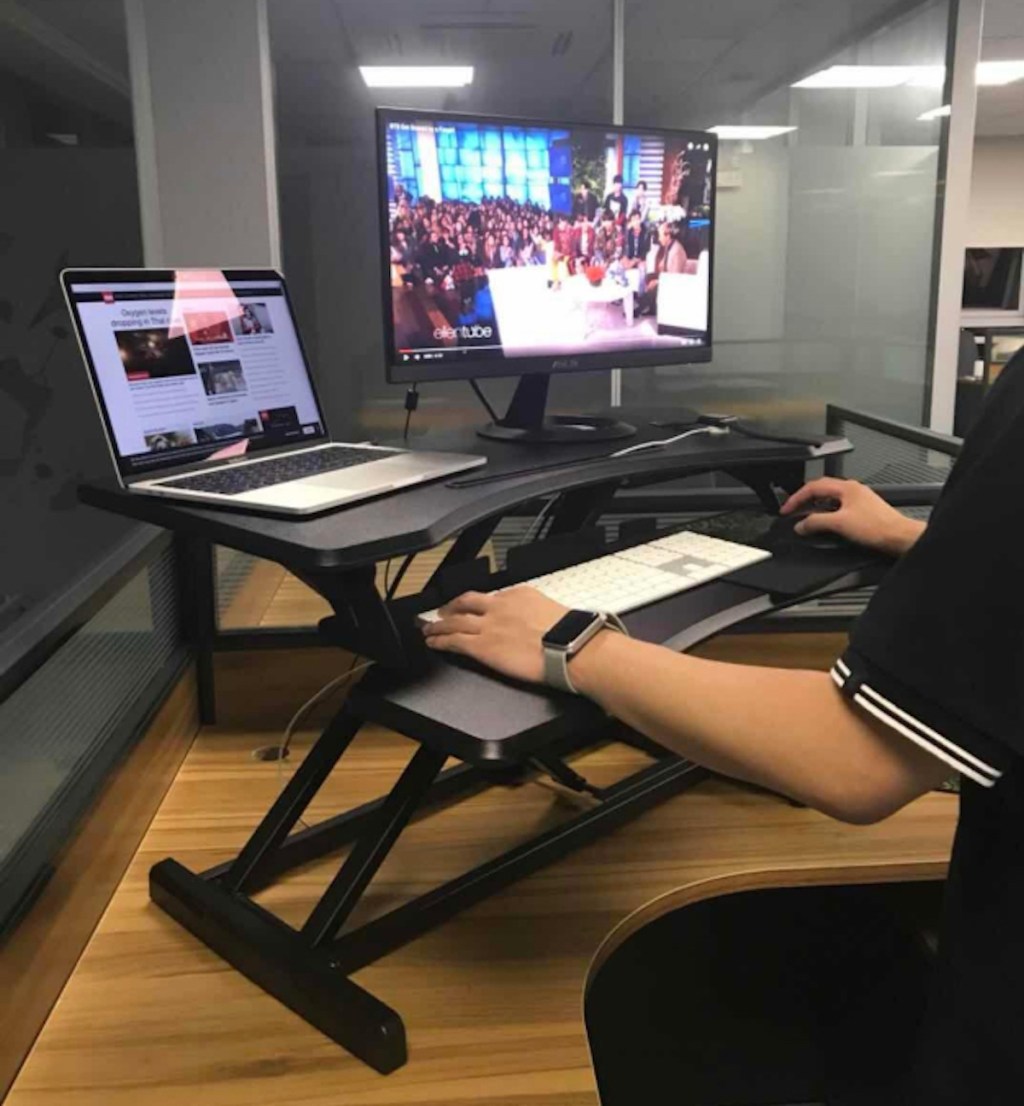 person standing at desk with onlineputer screen and laptop