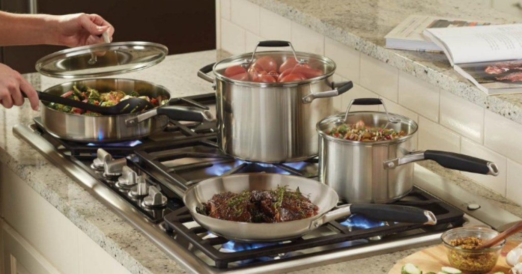 person removing lid from pot on the stove next to other pots