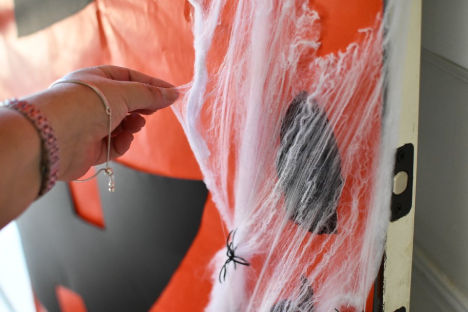 woman adding faux spiderwebs to DIY Halloween Front Door Decorations 