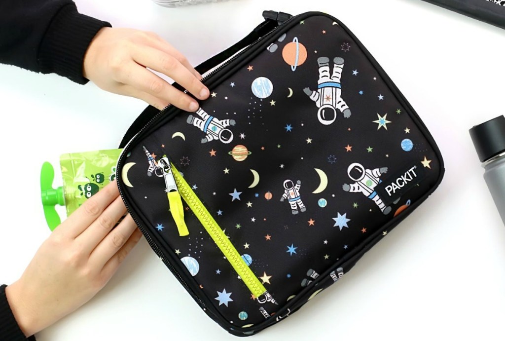 Hands taking applesauce pouch out of Astronaut print lunch bag