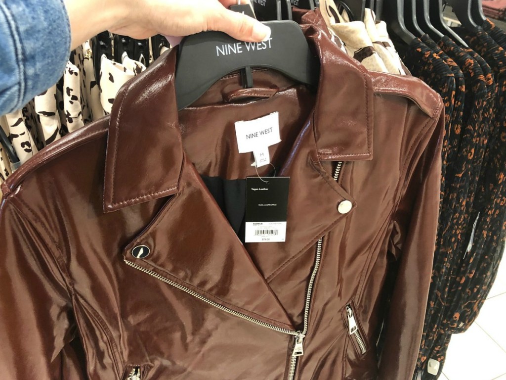 hand holding brown shiney jacket on hanger by store display