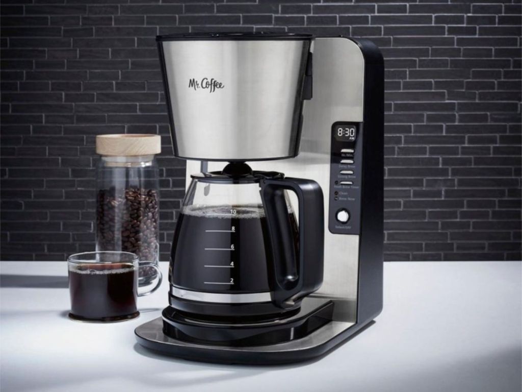 mr coffee stainless steel machine on counter cup of coffee and beans beside it