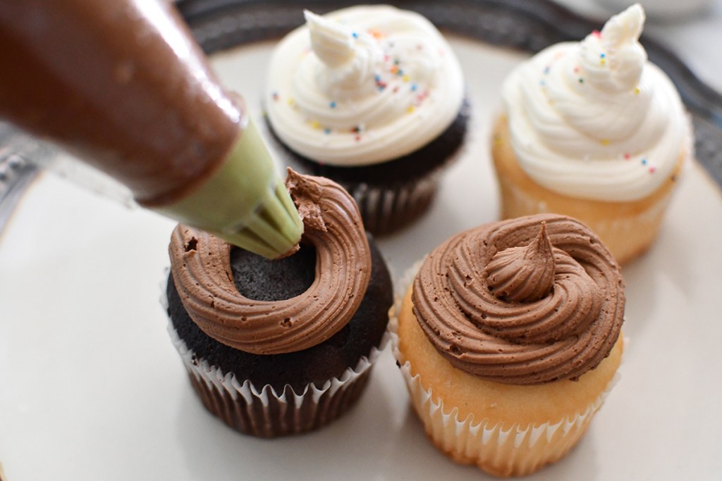 chocolate buttercream being piped onto cupcake