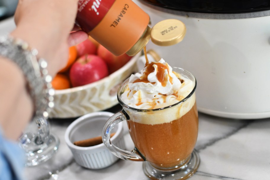 pouring caramel syrup over apple cider