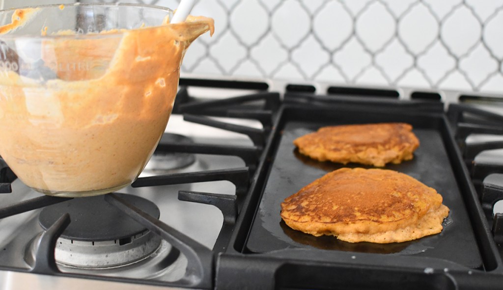 bowl of pumpkin pancake batter next to pancakes on griddle