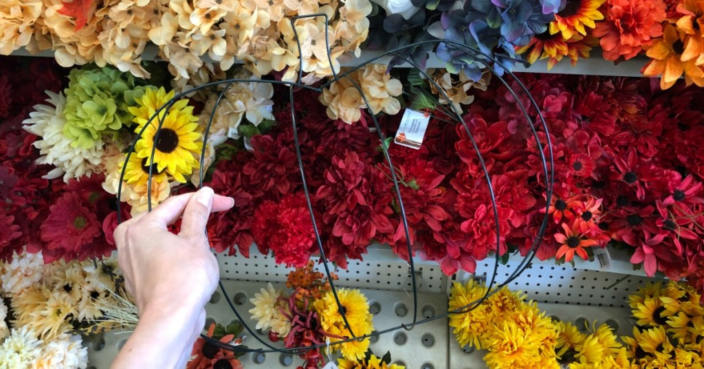 hand holding wire frame shaped like pumpkin in front of flowers