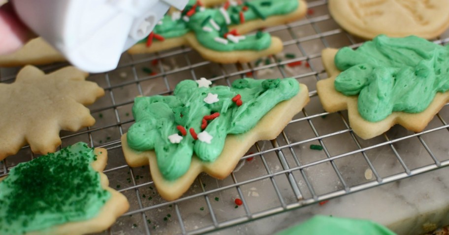 putting sprinkles on frosted Christmas cookie 