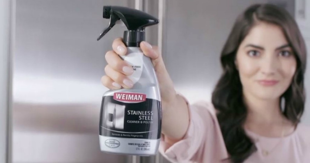 woman holding bottle of cleaner in front of appliance