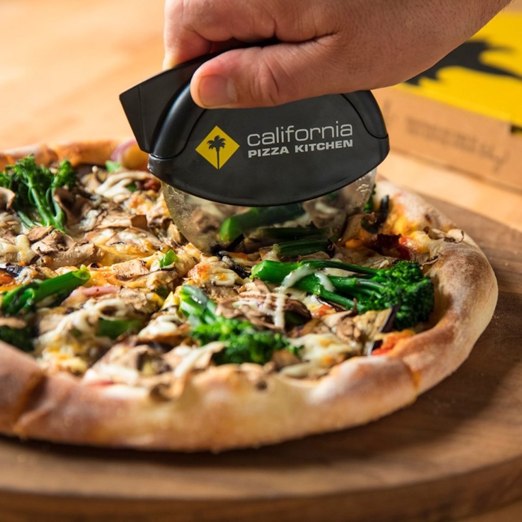 man slicing California Pizza Kitchen Pizza