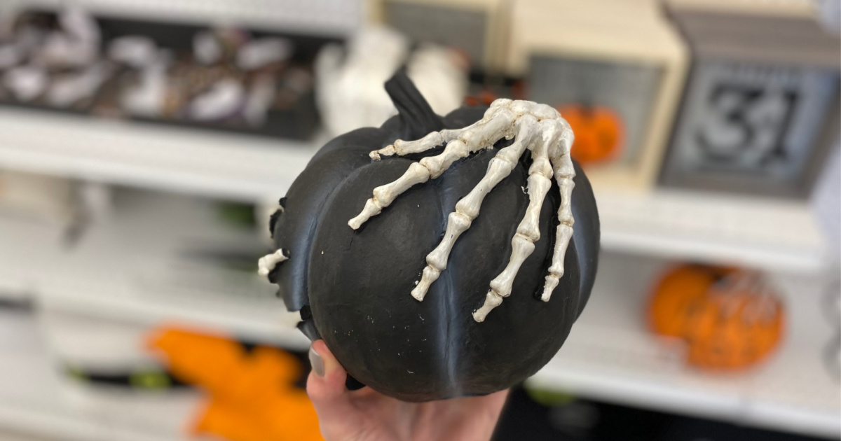 hand holding pumpkin with skeleton hand in store with blurry background