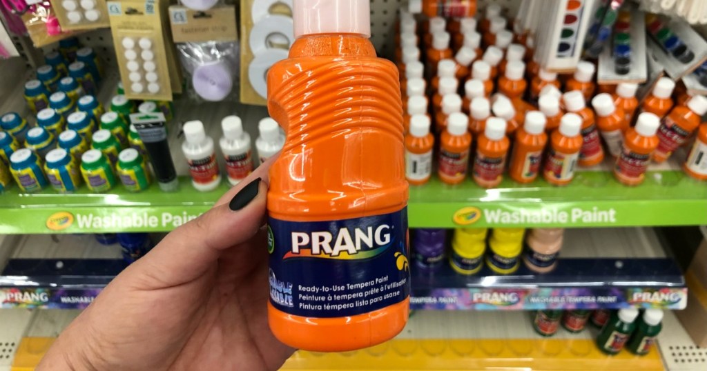 Woman holding Prang orange paint bottle in Dollar Tree