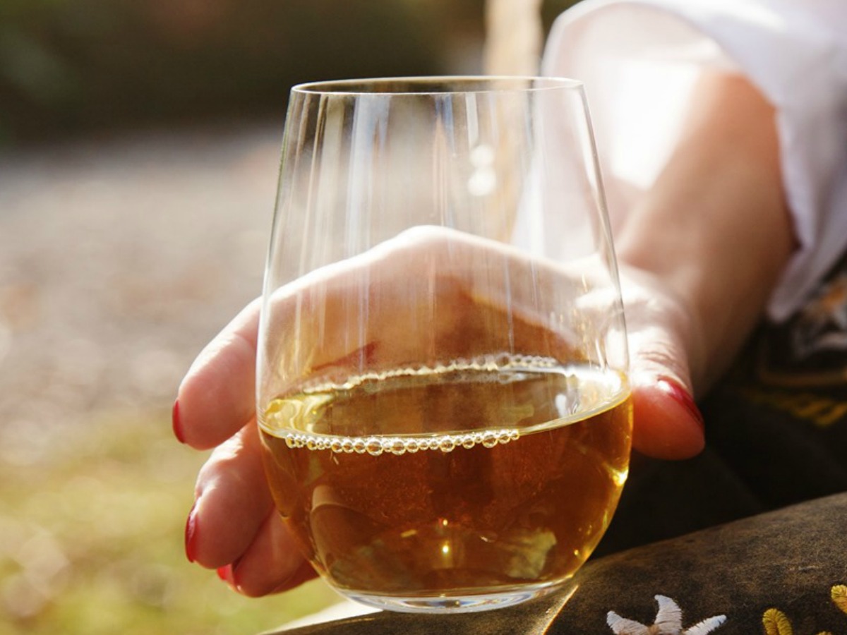 woman's hand holding a Riedel Wine Tumbler filled with white wine