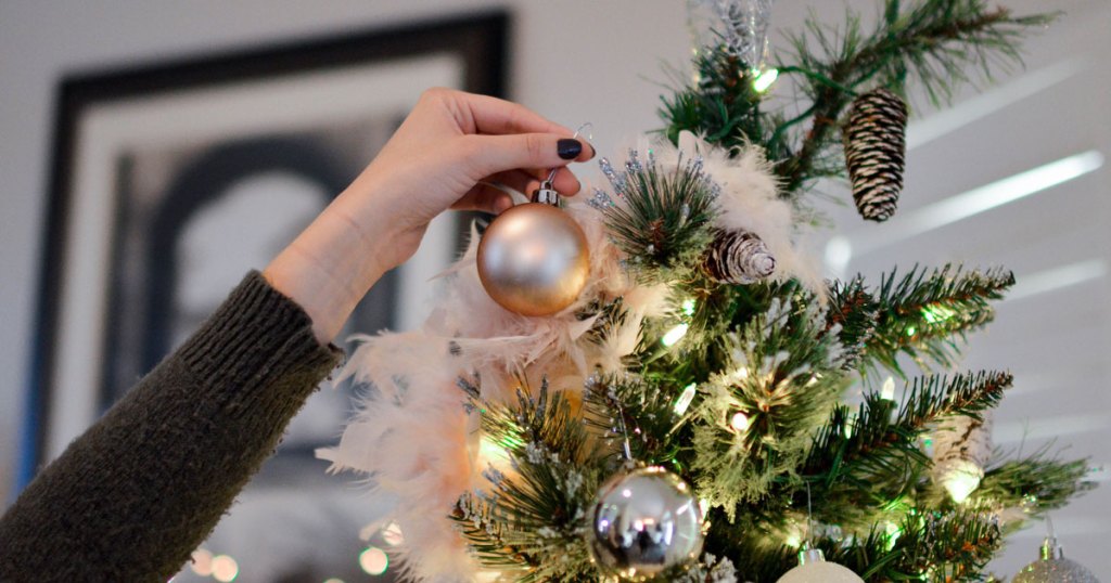 woman hanging ornaments onto a lit up christmas tree