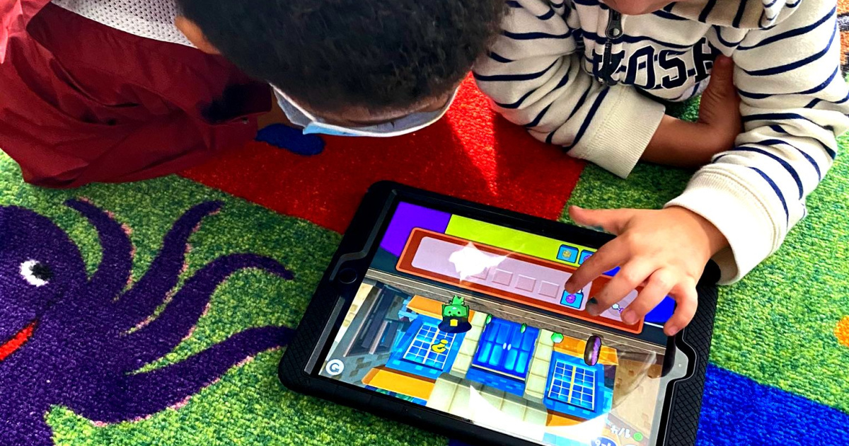 two kids playing tablet on floor