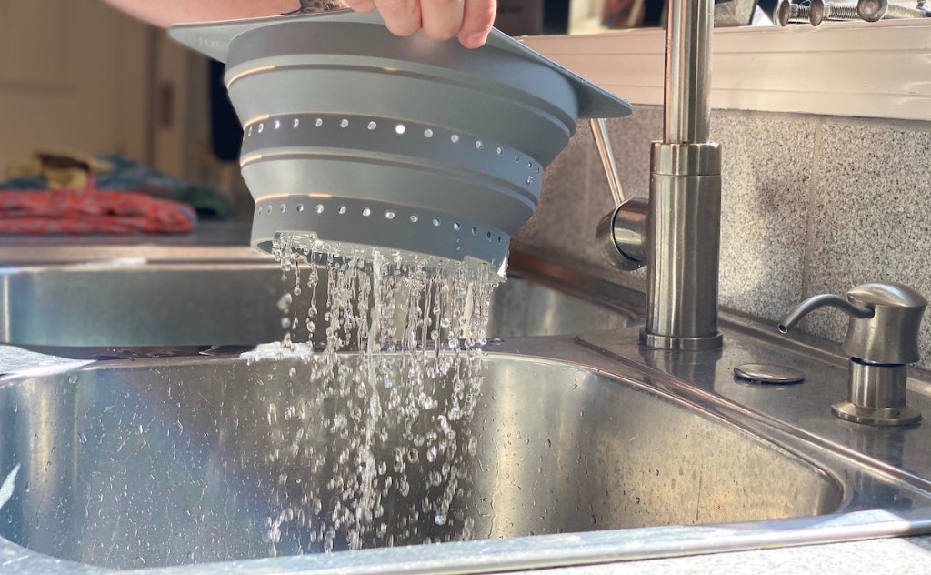 hands holding colander with water kitchen sink