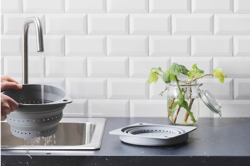 two colanders on kitchen counter with water running from sink