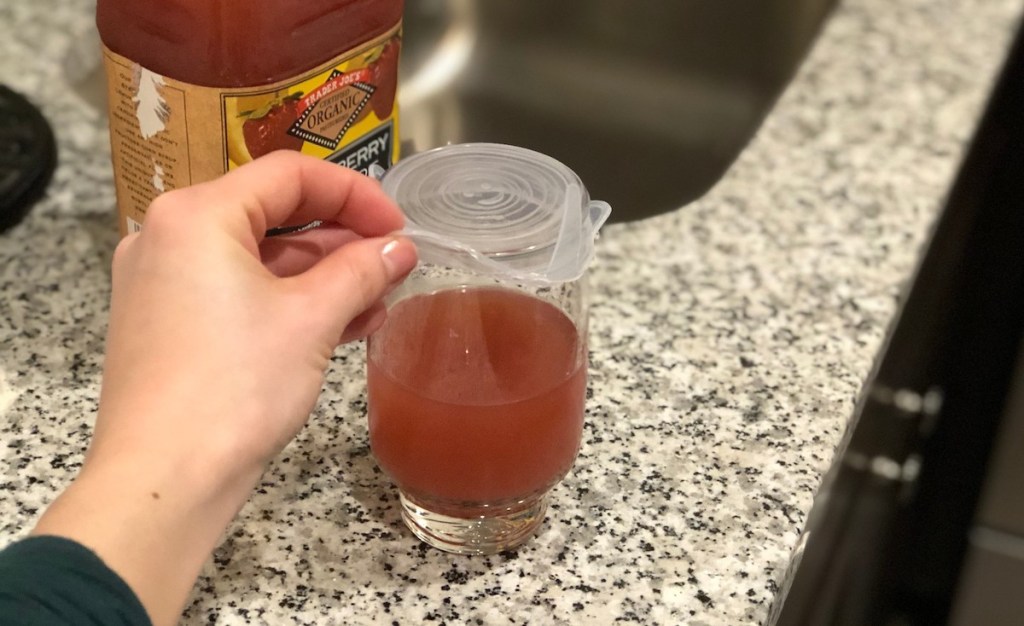 hand taking off silicone lid with pink juice in glass