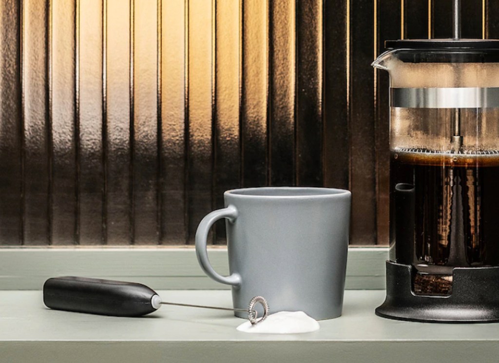 milk frother sitting on counter next to coffee mug and french press