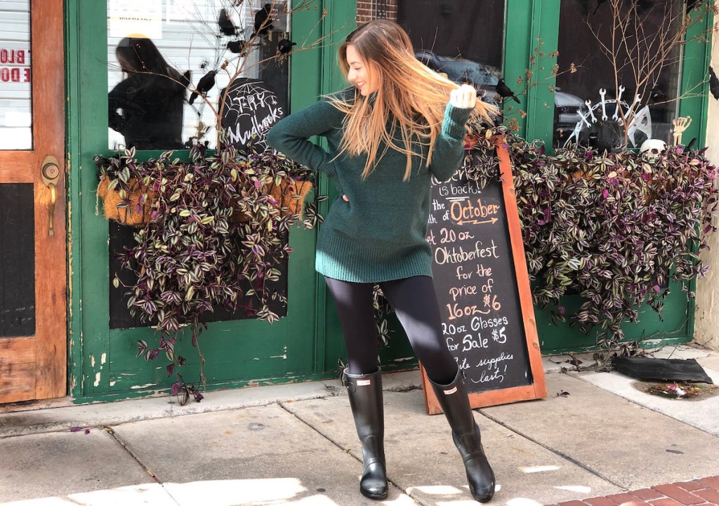 woman laughing wearing green amazon sweater and black leggings hunter boots