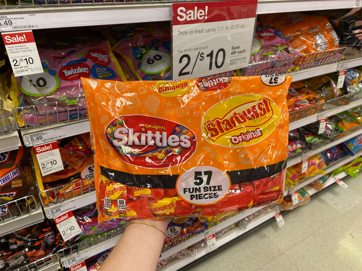 hand holding bag of skittle and starburst halloween fun size candy