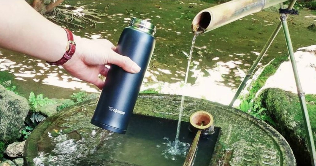 hand holding mug near stream catching water