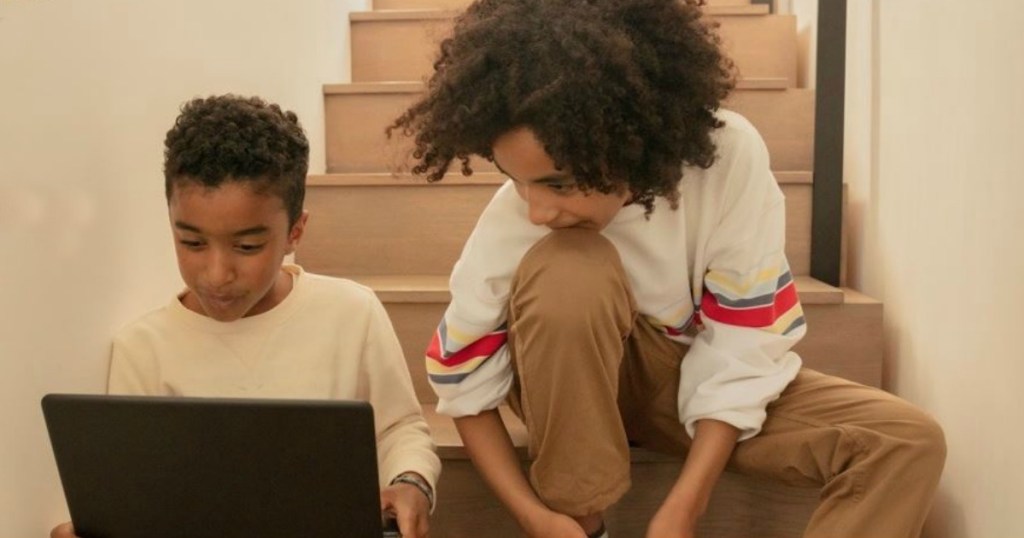 two boys sitting on stairs looking at latptop