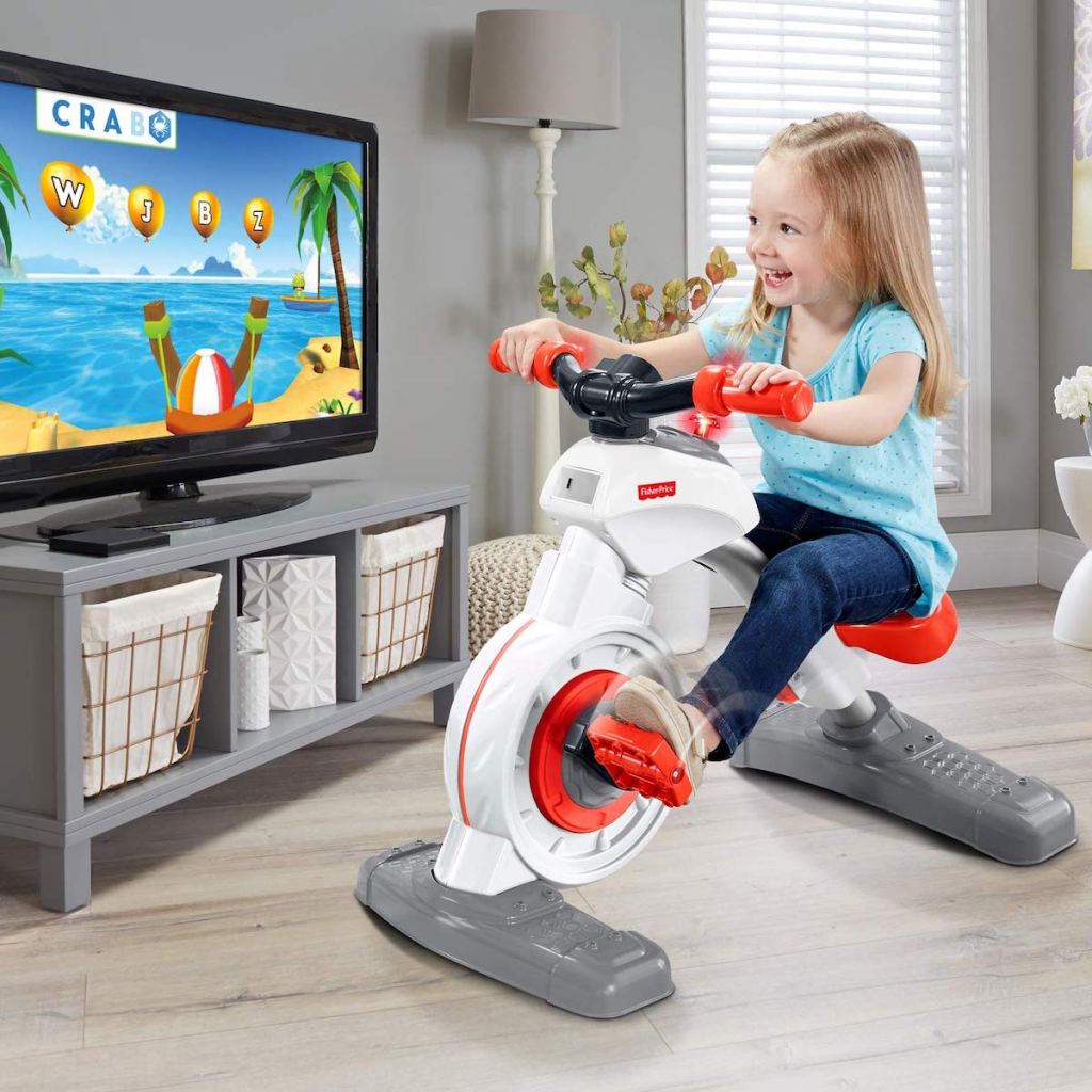 blonde girl riding on Fisher-Price Think & Learn Smart Cycle in living room with tv on