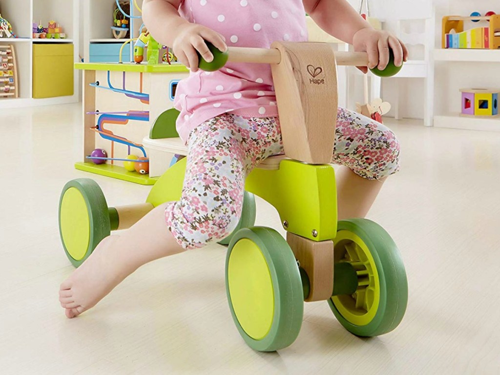 Young girl riding a wooden Hape ride on skooter