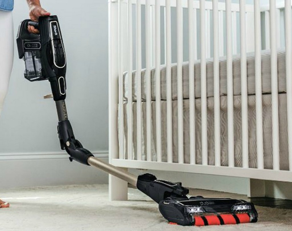 Woman using a Shark Handheld vacuum under a crib in a nursery