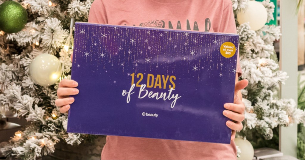 woman wearing a pink shirt holding Target 12 Days of Beauty advent calendar box in front of white christmas tree inside target