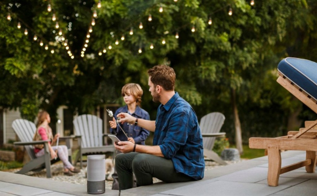 man and little boy roasting marshmallows in a yard next to a speaker