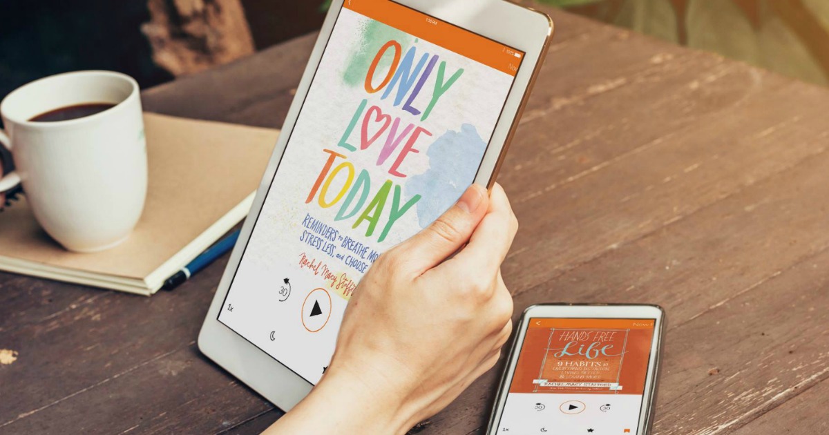 hand holding tablet playing audiobook next to cell phone and coffee