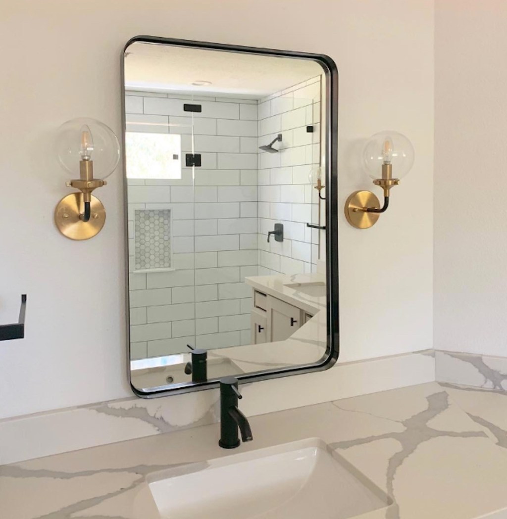 black rectangular mirror hanging in bathroom above sink and next to gold globe sconces