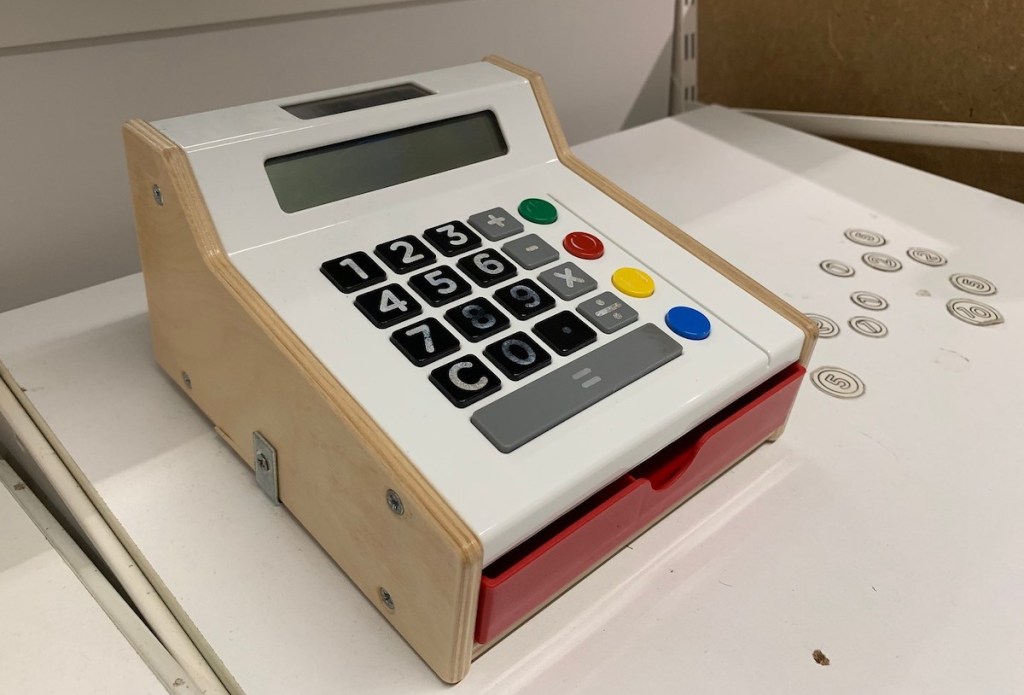 wooden toy cash register on white IKEA shelf with coins